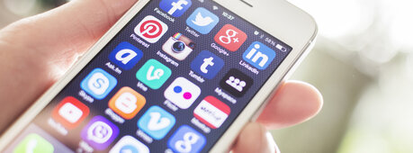 Nahaufnahme eines Smartphones, das in einer Hand gehalten wird. Auf dem Display ist der Startbildschirm mit verschiedenen Apps zu sehen.