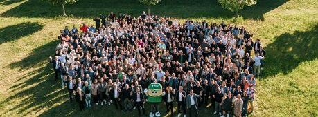 Etwa 300 wbg-Mitarbeitende stehen auf einer Wiese und winken in die Kamera.
